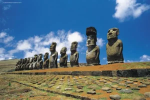 Alignement de quinze Moai sur la plateforme de Tongariki sur l'île de Pâques, sous un ciel bleu parsemé de nuages.