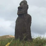 A solitary moai statue, standing in a grassy field under a cloudy sky on Easter Island.
