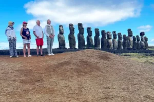 A group of tourists posing in front of a row of moai statues on Easter Island, under a partly cloudy blue sky.